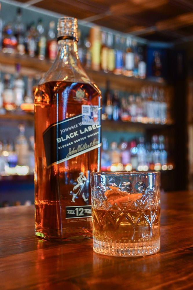 Bottle of Blanton's Single Barrel Bourbon Whiskey with its iconic horse-and-jockey stopper on a wooden bar at Highlands Lounge, with a tulip-shaped tasting glass beside it